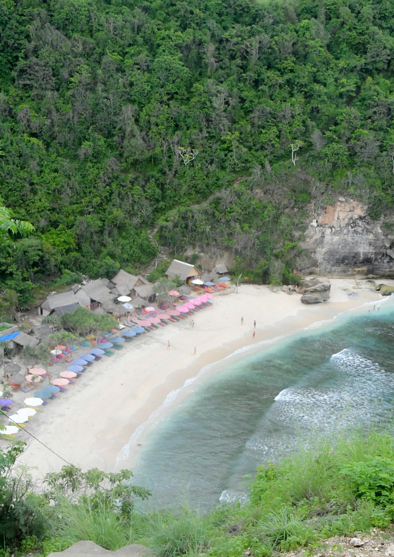 Atuh Beach seen from the hillside, with beach umbrellas along the sand