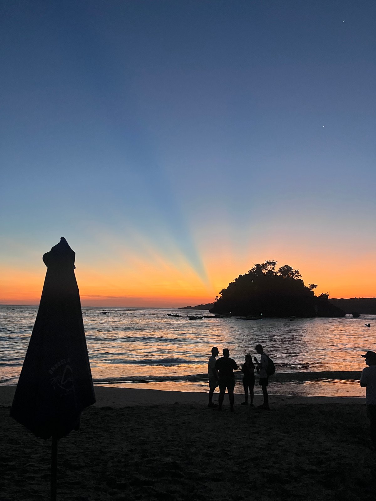 Visitors and a closed beach umbrella beneath the sunset sky at Crystal Bay.