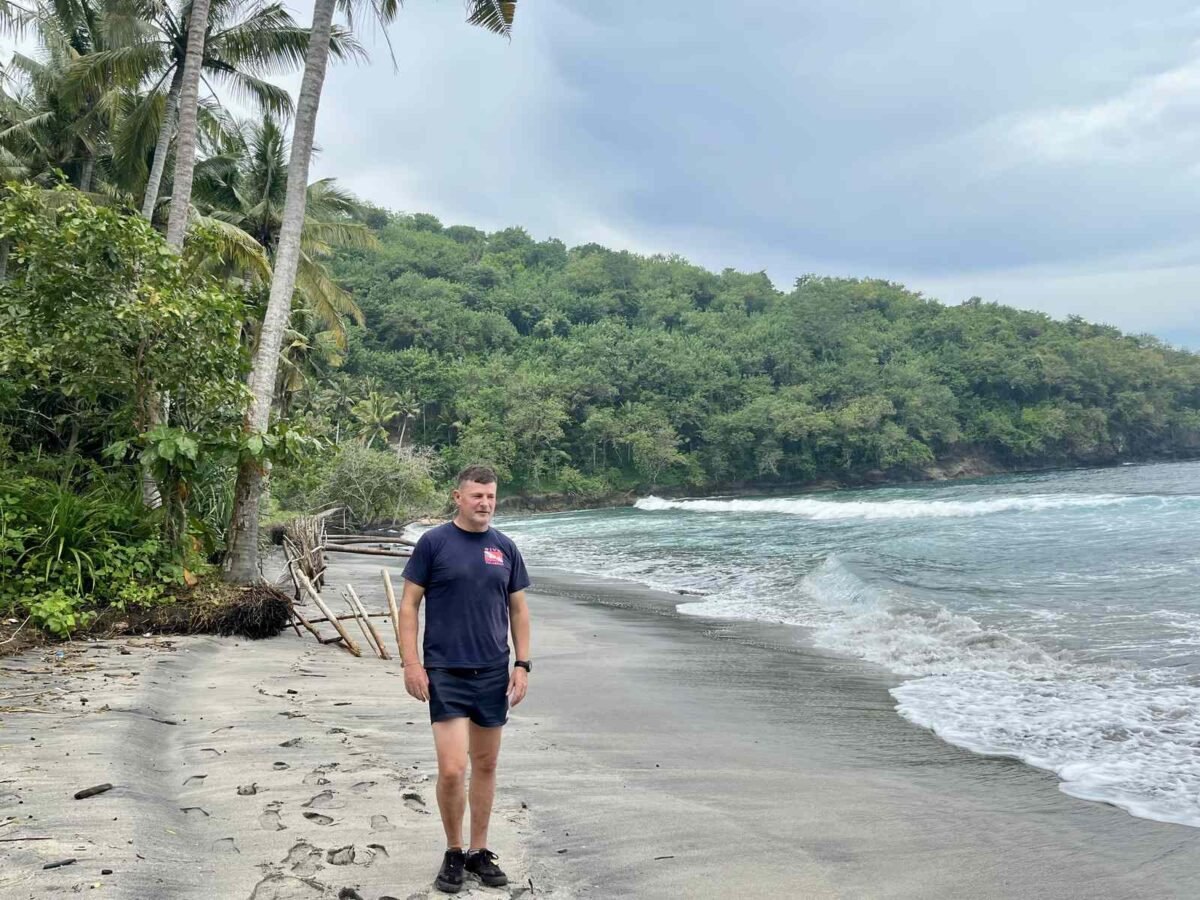 Blaise Jaeger on the sand at Gamat Bay with palms and wooded slopes