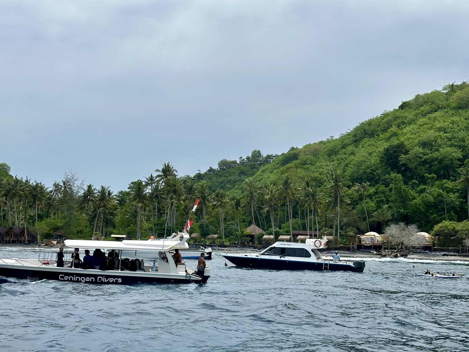 Boat and buildings along Gamat Bay beach beneath green slopes