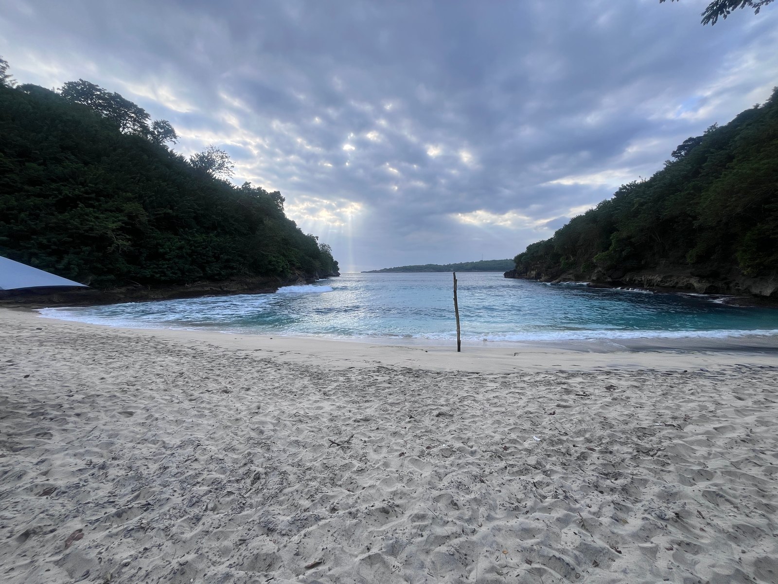 Pandan Beach sand between two wooded headlands, with waves at the shore