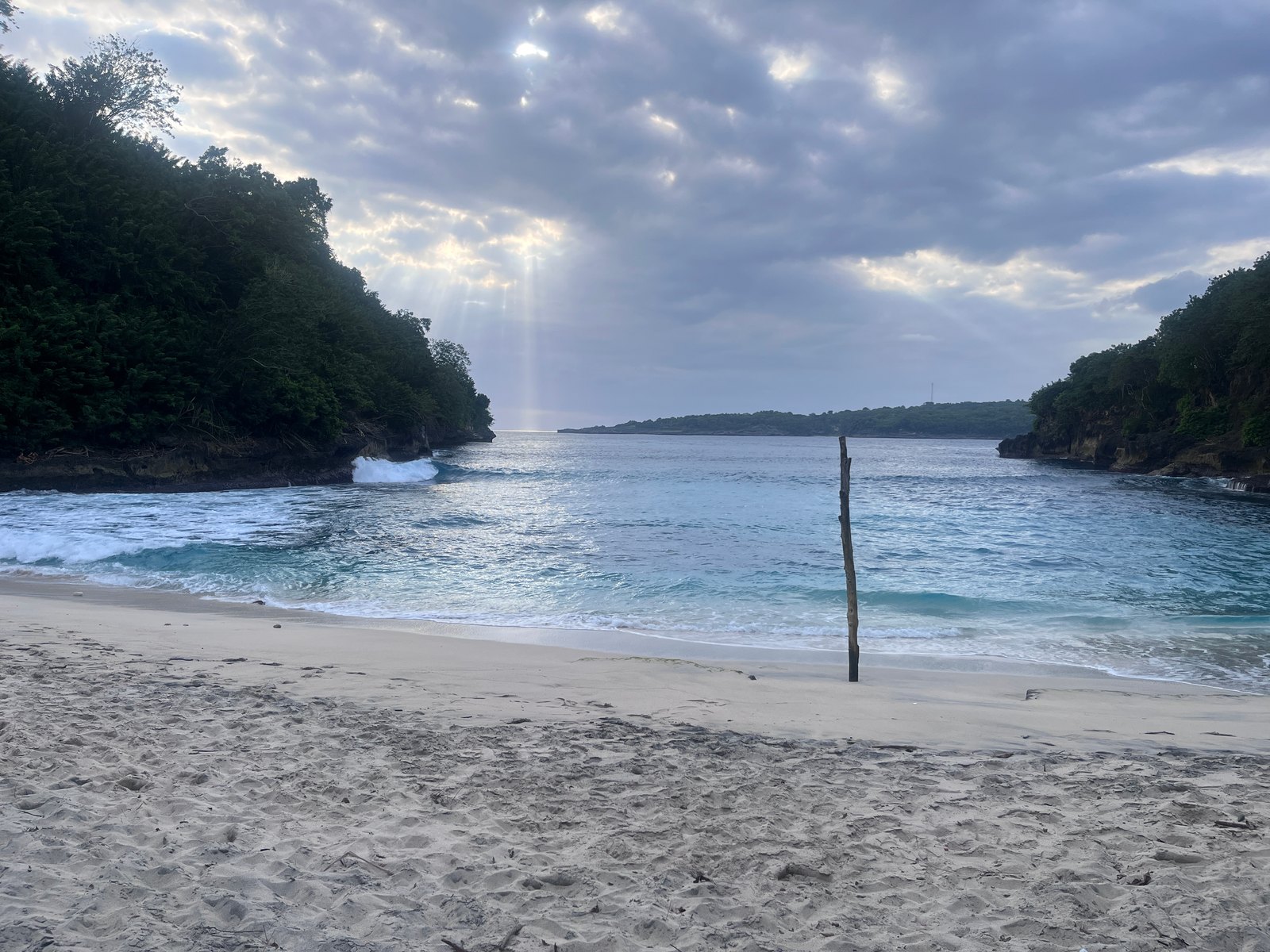 Waves rolling onto Pandan Beach beside a wooden pole in the sand.