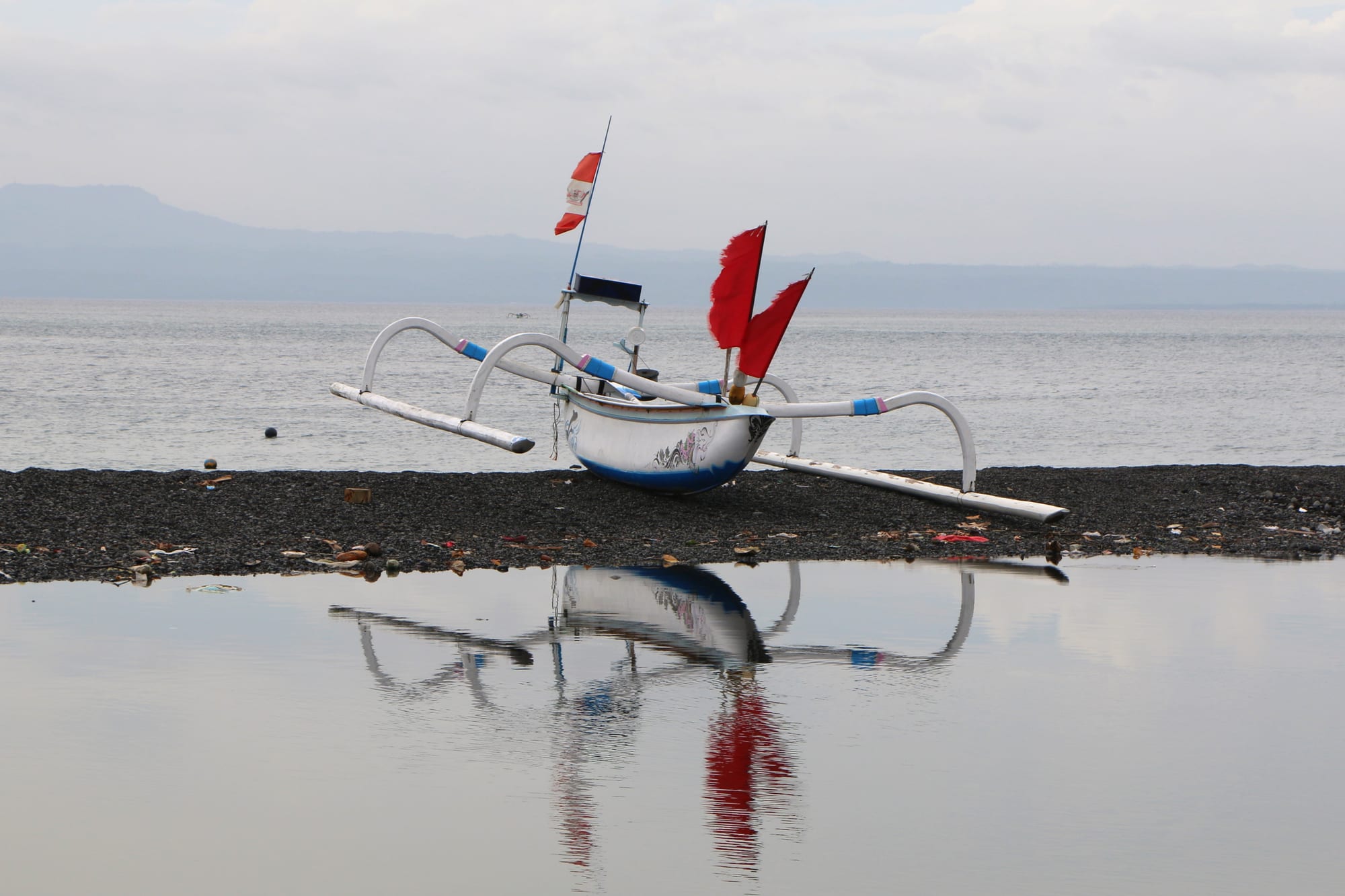 Bateaux traditionnels alignés le long de la côte de sable noir à Kusamba