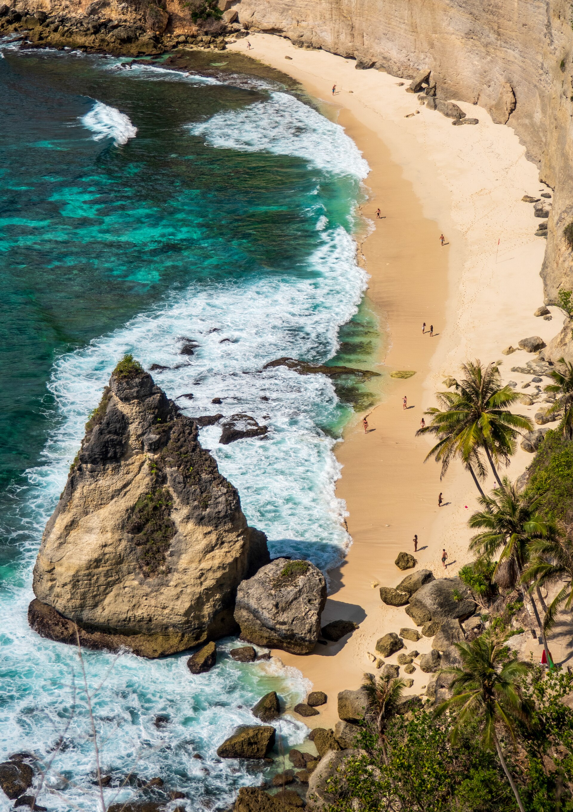 White sand beach below tall limestone cliffs in Nusa Penida