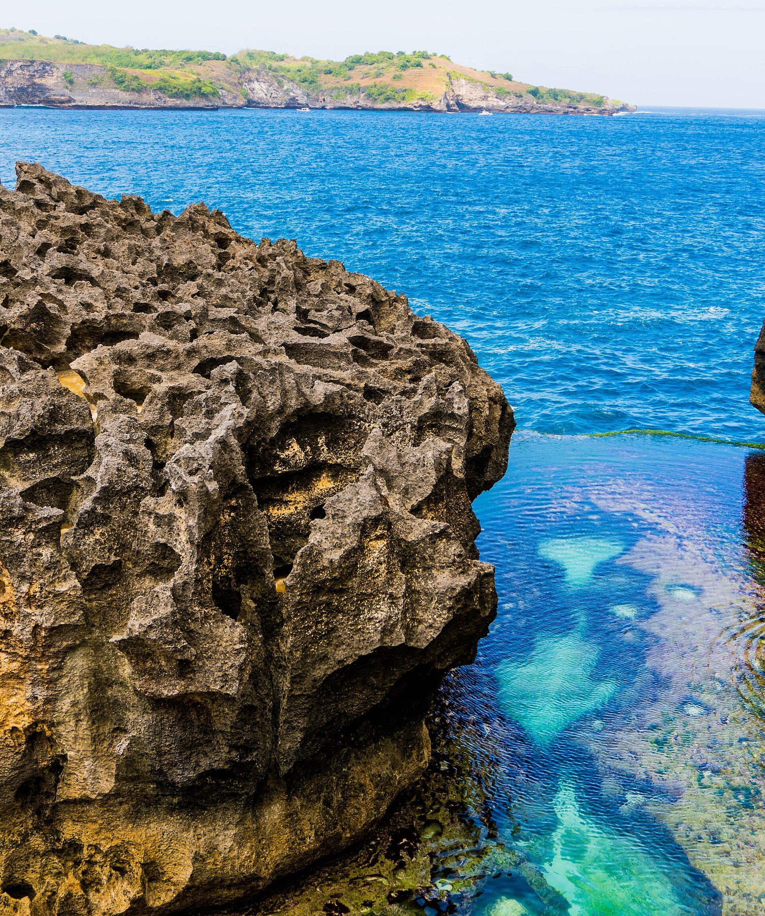 Clear, still water in Angel's Billabong beside a jagged limestone rock, with the open sea just past the pool's edge.