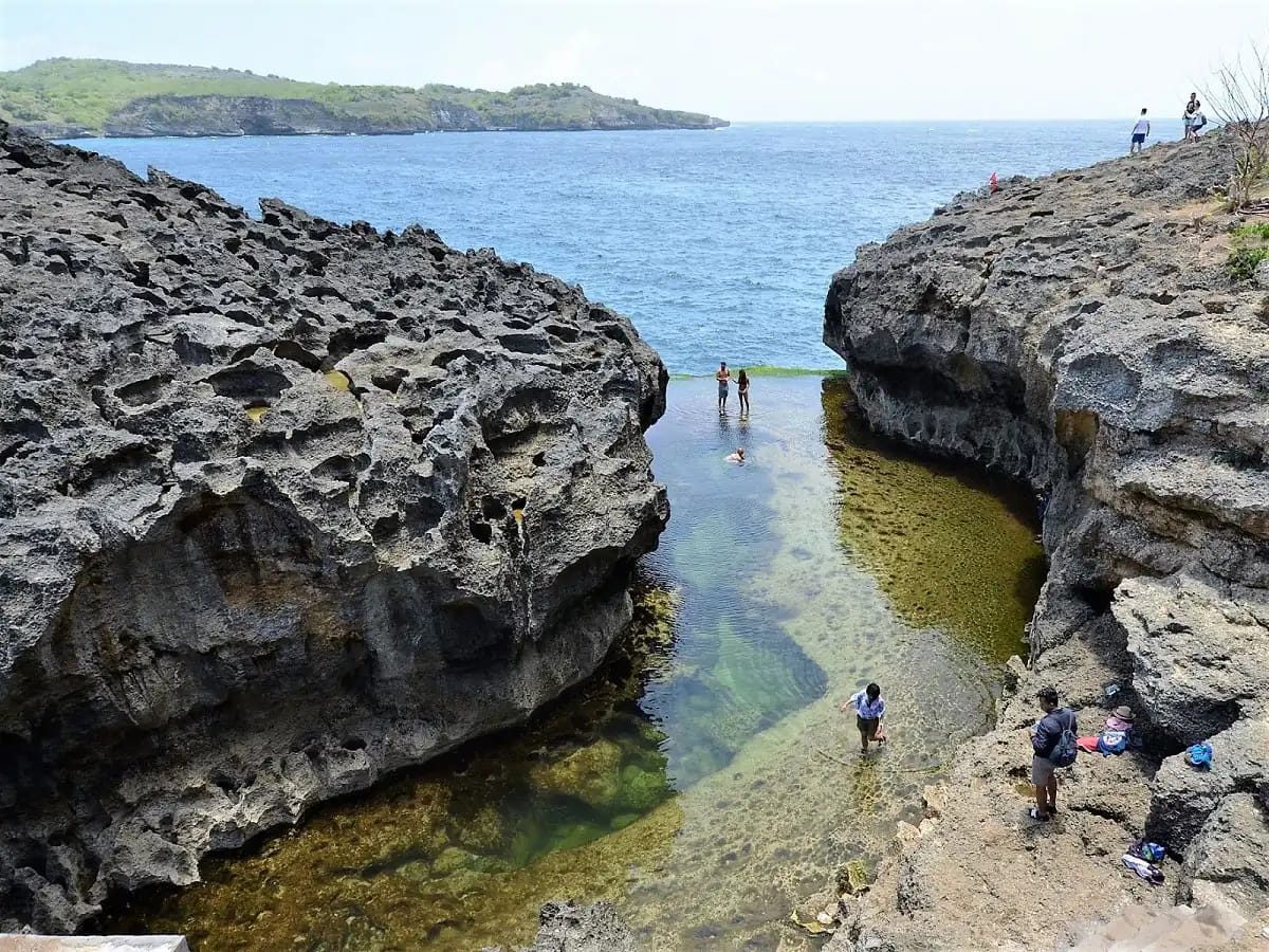 People wading in Angel's Billabong between two rock walls, with more visitors on the rocks above.