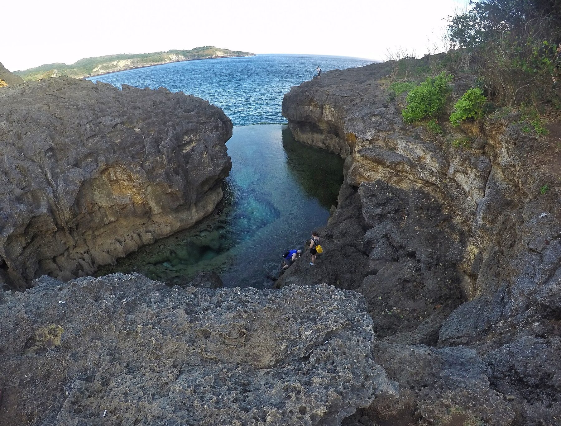 The narrow rock channel of Angel's Billabong seen from above, with two people climbing down to the water.