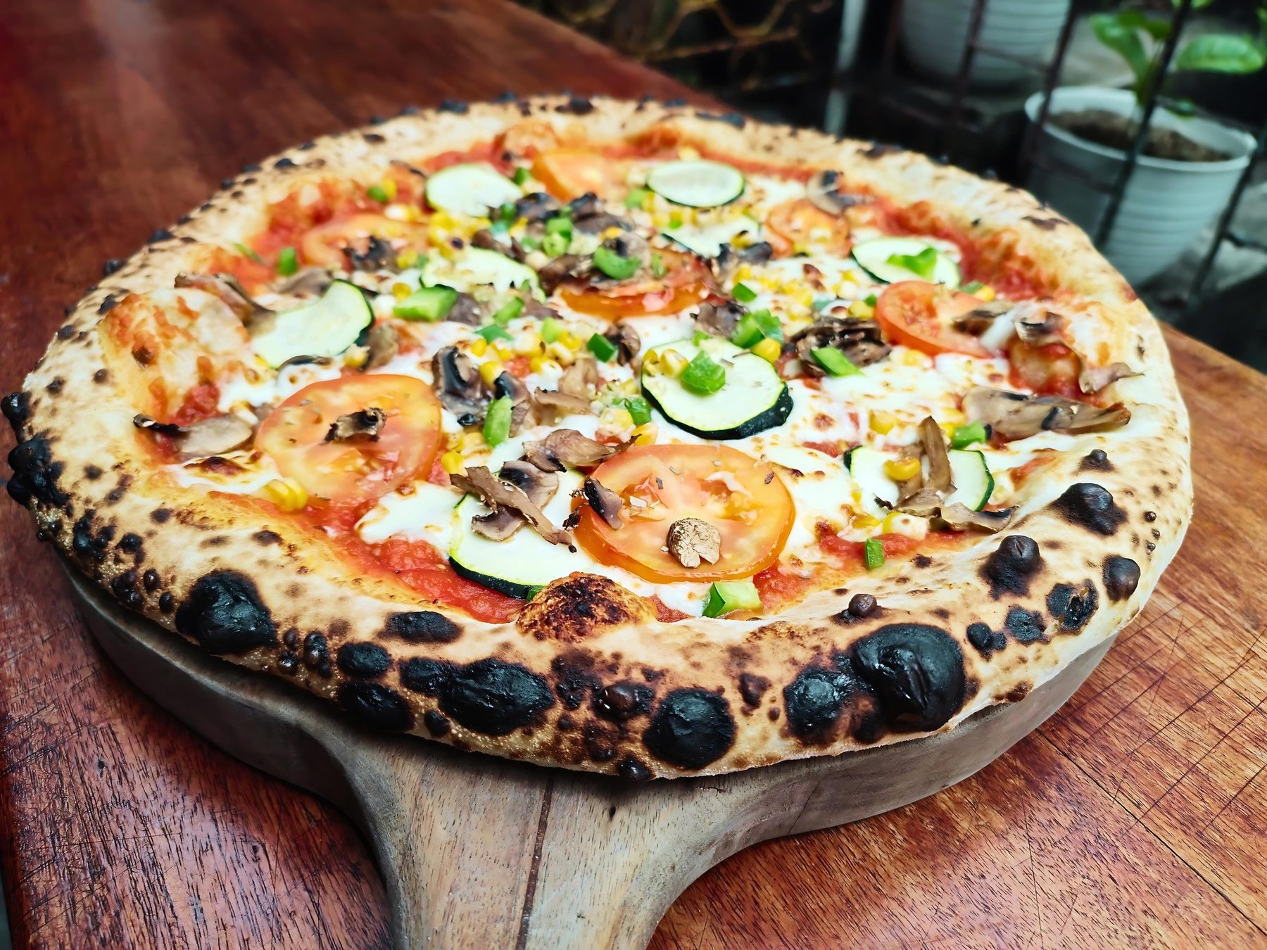 Vegetable pizza with zucchini, tomato, mushroom and peppers on a wooden board at Artrolling Bistro