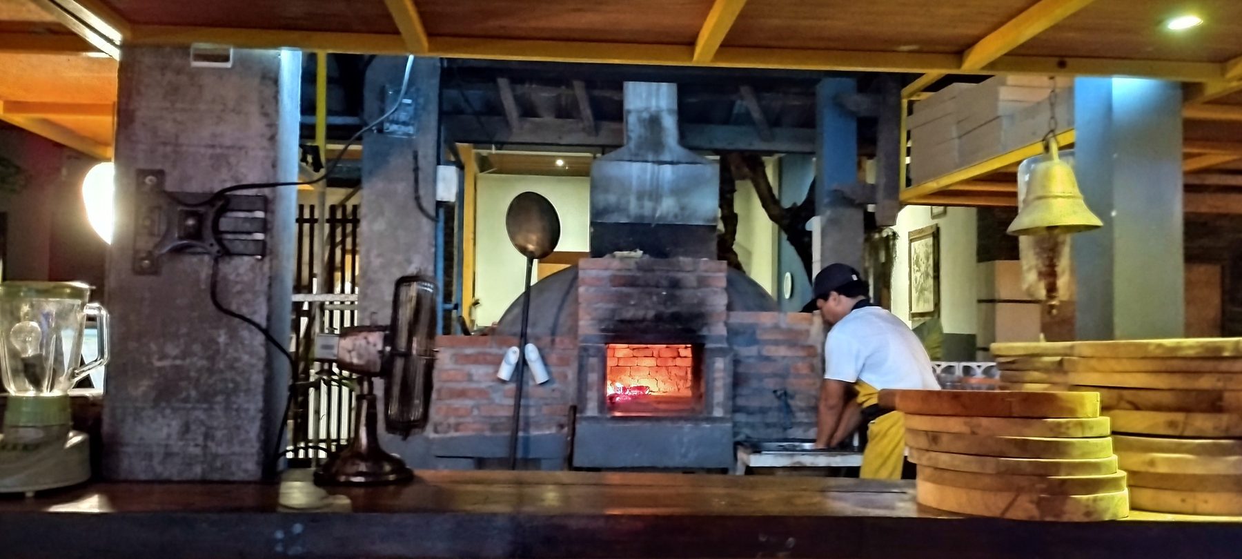 Brick wood-fired pizza oven with a fire burning inside the open kitchen at Artrolling Bistro