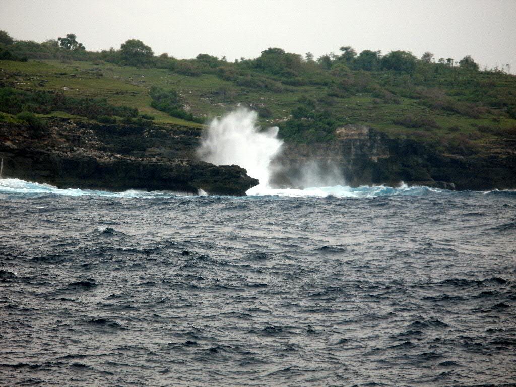 Rough grey sea and breaking waves against the rocky Nusa Penida coast under a cloudy sky
