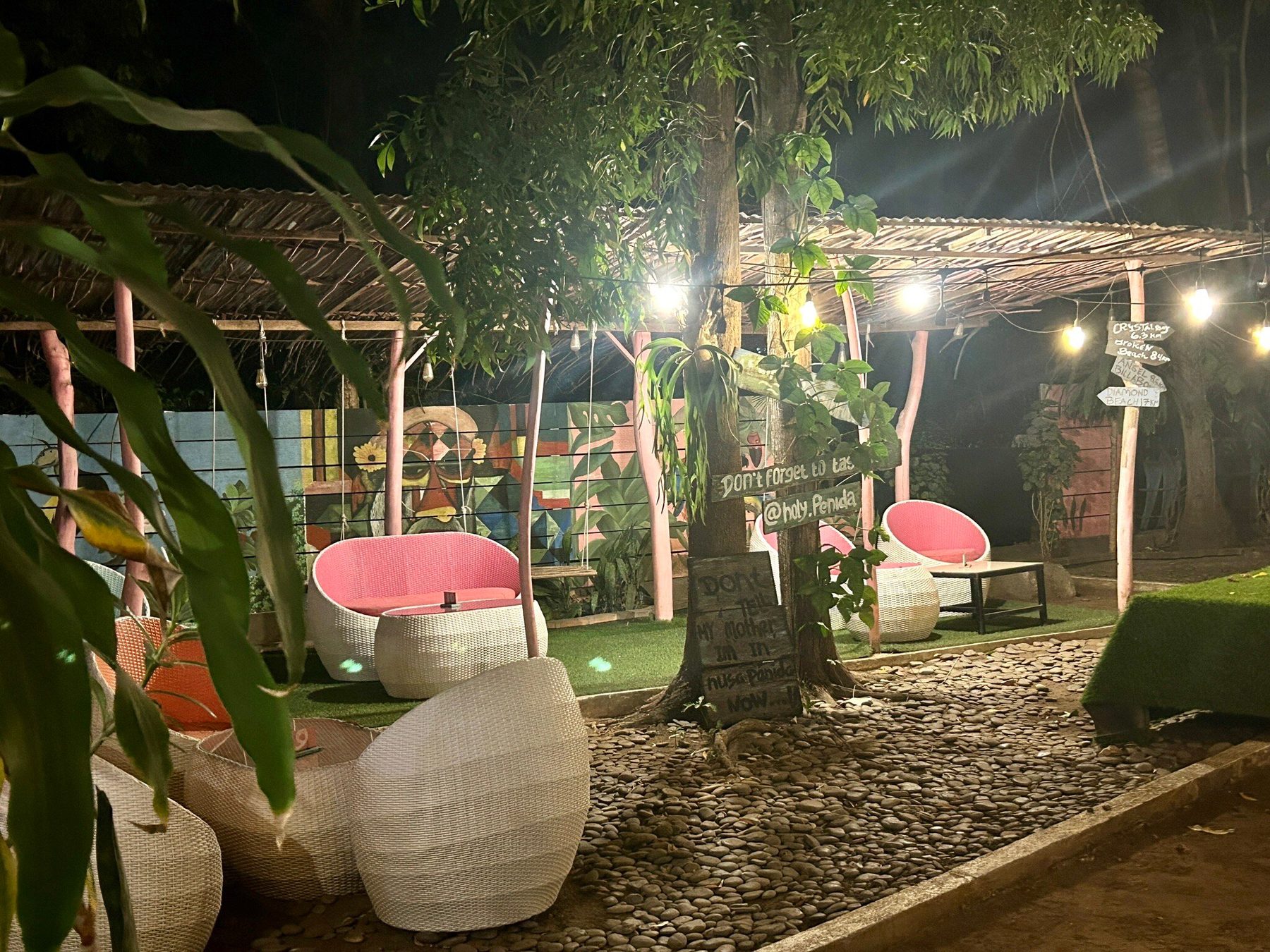 Garden lounge at Holy Penida with egg-shaped chairs, string lights and a chalkboard under the trees at night