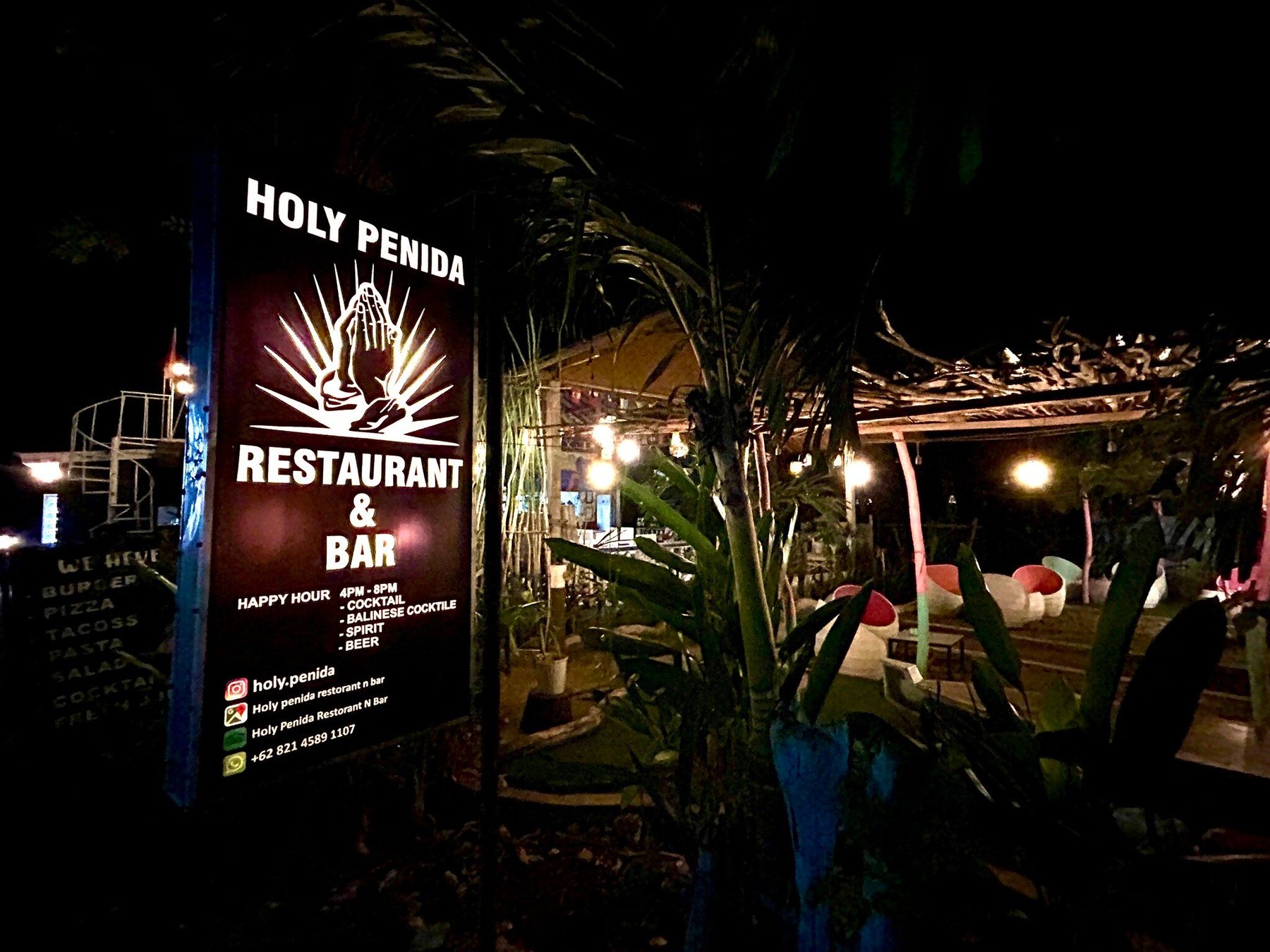 Lit Holy Penida Restaurant and Bar sign at night beside the garden seating