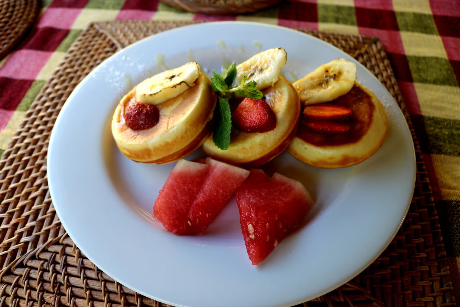 Plate of small pancakes topped with banana and strawberry, served with watermelon at Kavana Penida