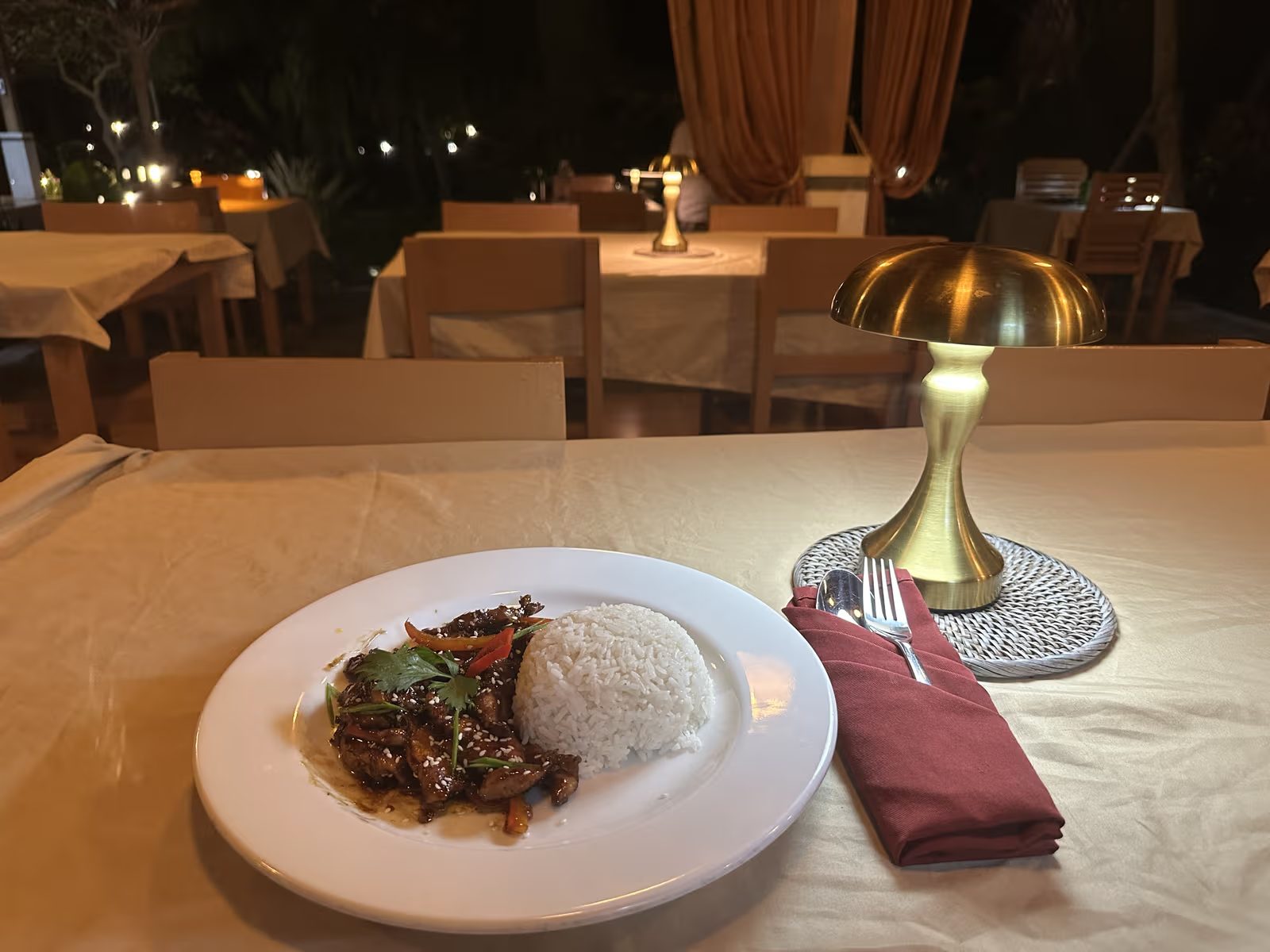 Evening table at Kavana Penida with a rice plate, a gold table lamp and white tablecloths