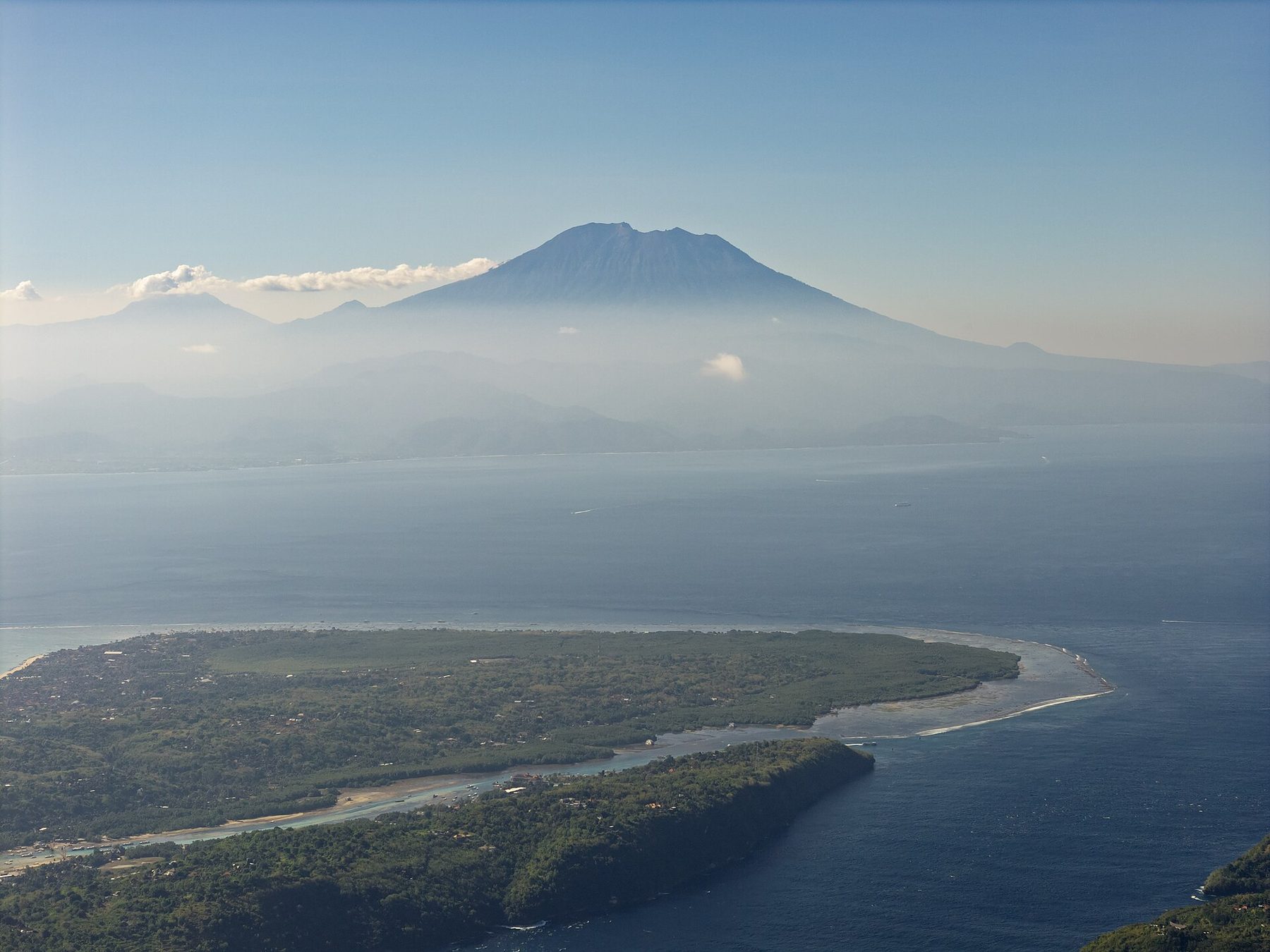 Aerial view of Nusa Lembongan and Nusa Ceningan, separated by a narrow channel, with Mount Agung on Bali rising behind across the strait.