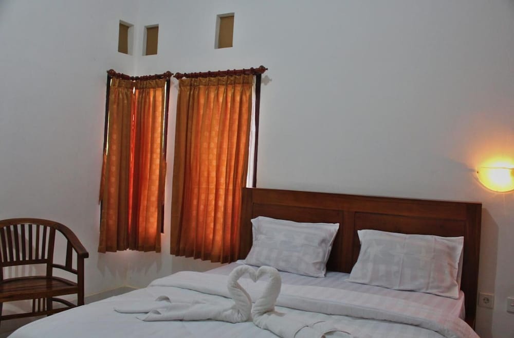 Double bed with white linen, towel swans and orange curtains at Nyuh Kadah Guest House