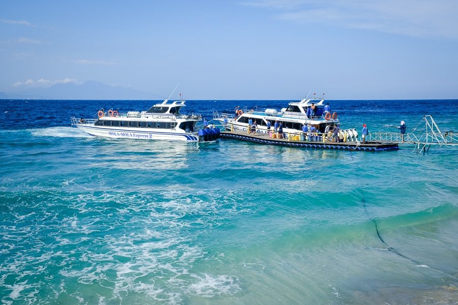 Two fast boats beside a floating jetty off the beach at Sampalan, with turquoise water in front.
