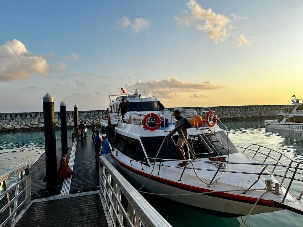 Crew tying up a fast boat at the floating pier inside Sampalan harbour's stone breakwater at dusk.