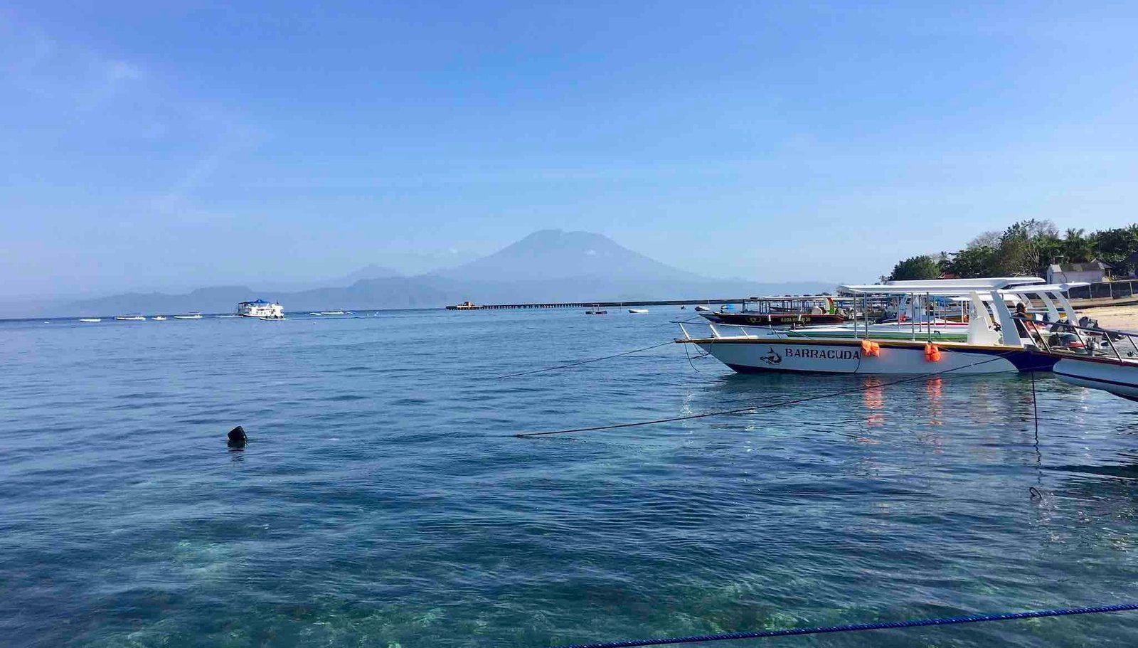 Snorkeling boats moored in clear water off Toyapakeh, with Mount Agung on the horizon.